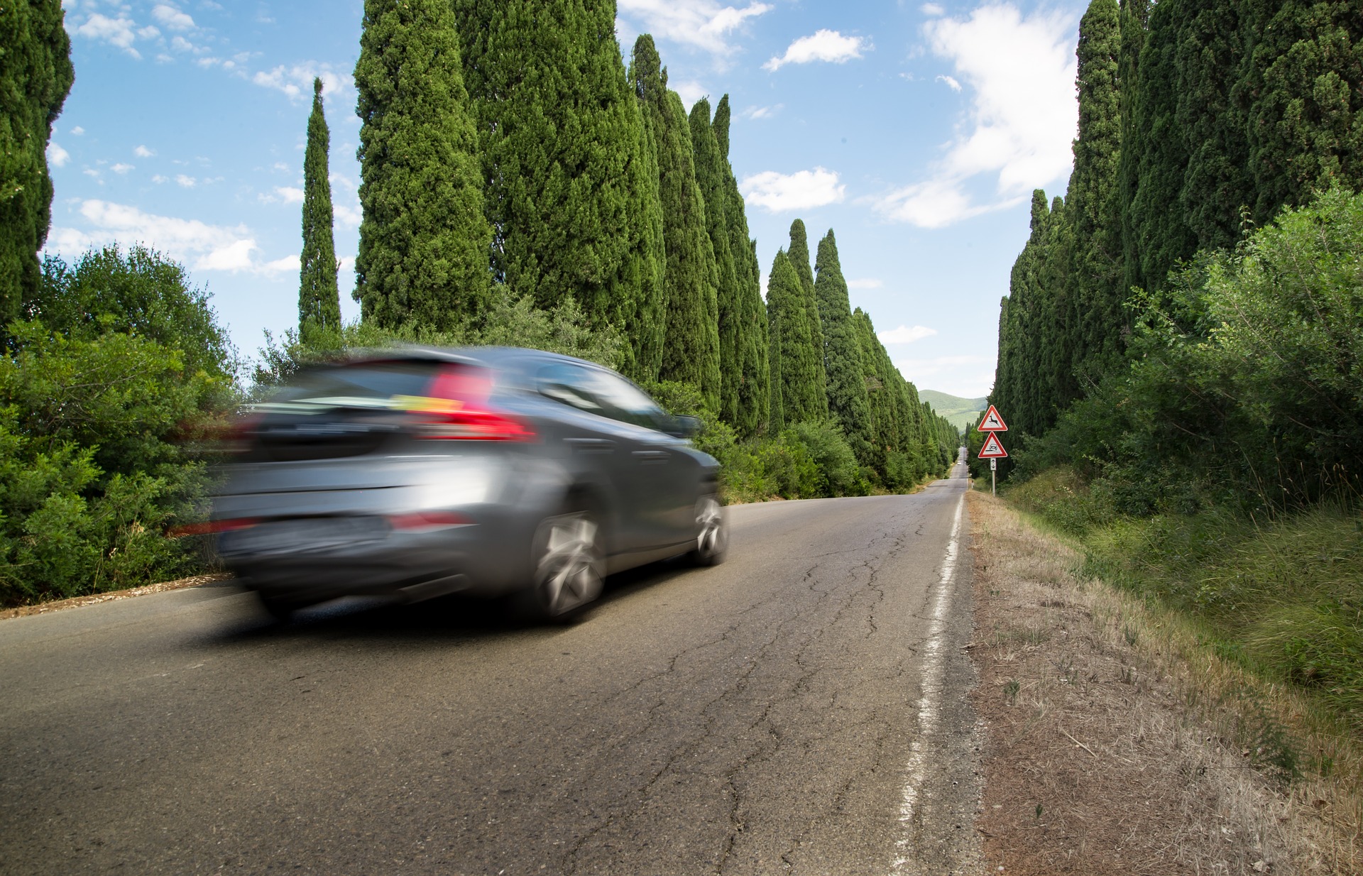 Voiture familiale en mouvement qui roule sur une route bordée de cyprès